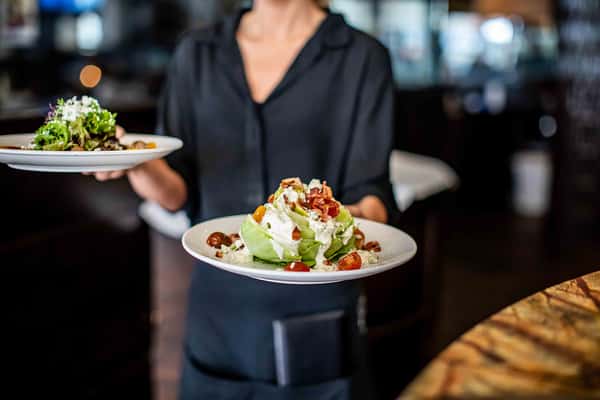 A server presents a fresh, beautifully plated salad, highlighting a refined and welcoming dining experience.