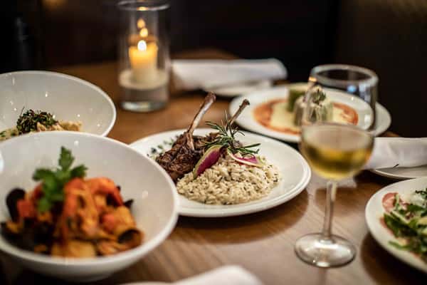 A cozy table setting showcases a plate of pasta topped with fresh herbs, paired with a glass of white wine and soft candlelight. The warm ambiance creates an intimate and inviting dining experience, perfect for enjoying classic Italian flavors.