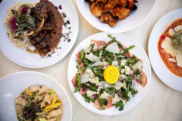 An overhead view of a vibrant spread of dishes, featuring a fresh salad topped with a bright egg yolk, alongside other plates of pasta and savory items. The presentation is colorful and abundant, showcasing a variety of textures and ingredients typical of a rich Italian dining experience.