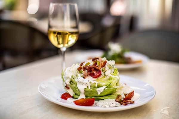 A fresh wedge salad topped with creamy dressing, crispy bacon, and tomatoes, paired with a chilled glass of white wine for a refreshing bite.
