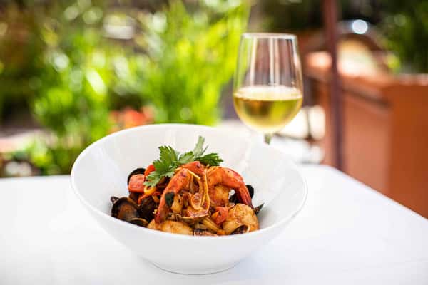 A vibrant pasta dish tossed with seafood and fresh herbs, served with a glass of white wine in a bright, inviting setting.
