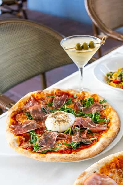 A classic Italian pizza topped with cured meats and fresh greens, served alongside a crisp martini for a stylish dining experience.