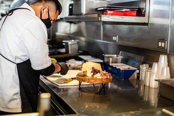 A chef works intently in a professional kitchen, carefully plating a dessert or specialty dish. The stainless-steel workspace and organized ingredients emphasize precision, cleanliness, and the dedication behind each creation.