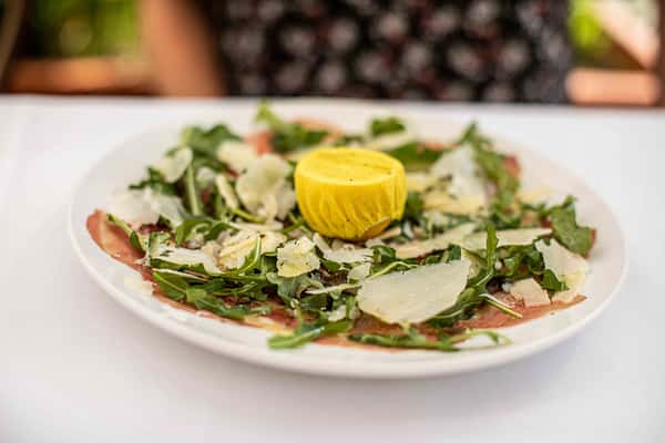 A fresh, vibrant salad topped with shaved cheese and a bright citrus garnish, beautifully presented for a light and flavorful start.