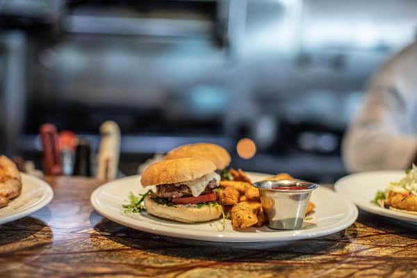 A juicy gourmet burger served with crispy fries and dipping sauce, plated in a casual yet polished dining atmosphere.