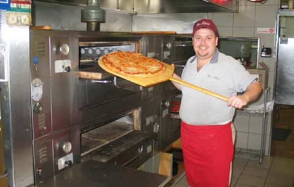 Man holding cheese pizza on a pizza paddle infront of an oven