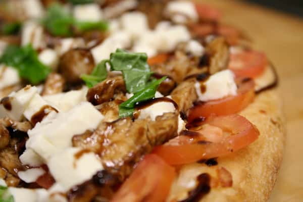 Pizza topped with Fresh mozzarella, basil, chicken, and tomatoes