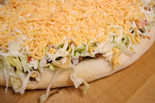 Pizza with lettuce and shredded cheddar cheese on wooden table
