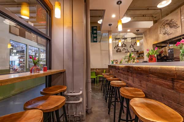 Cozy modern pizza and pasta bar with wood accents, pendant lighting, bar stools, and fresh floral decor along the counter.
