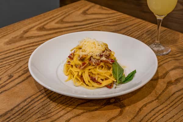 Spaghetti carbonara topped with grated cheese and garnished with basil, served on a white plate.