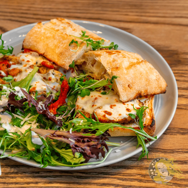 Toasted sandwich with melted cheese, chicken, and herbs, served with a side of mixed greens and creamy dressing.