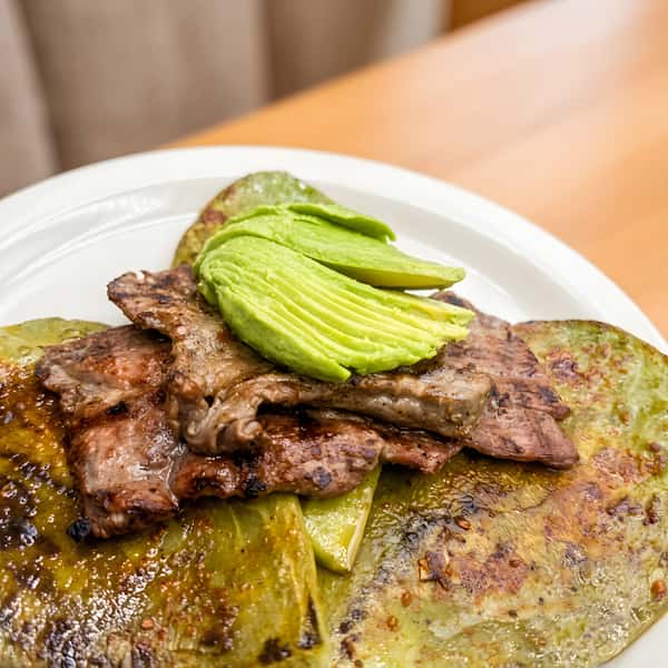 Carne asada served with grilled onions and avocado slices on a white plate.