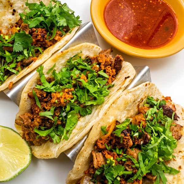 Beef tacos topped with cilantro and onions, served with lime and salsa.