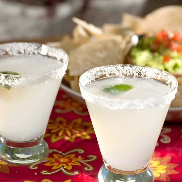 Two lime margaritas with salted rims on a colorful table setting.