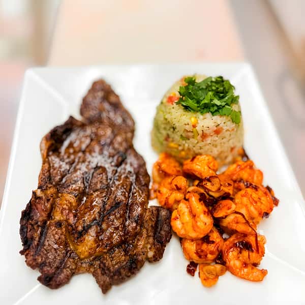Grilled steak and shrimp served with rice and sautéed vegetables on a white plate.
