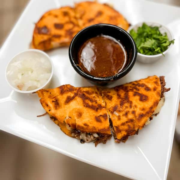 Quesadilla slices served with dipping sauce, onions, and cilantro.