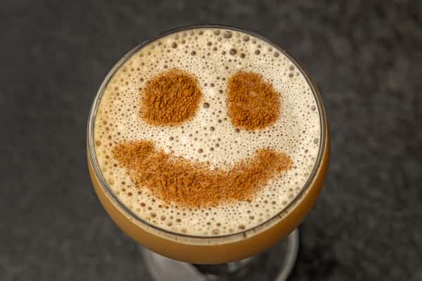 Frothy espresso martini topped with a cinnamon smiley face design, adding a playful touch to this creamy cocktail.