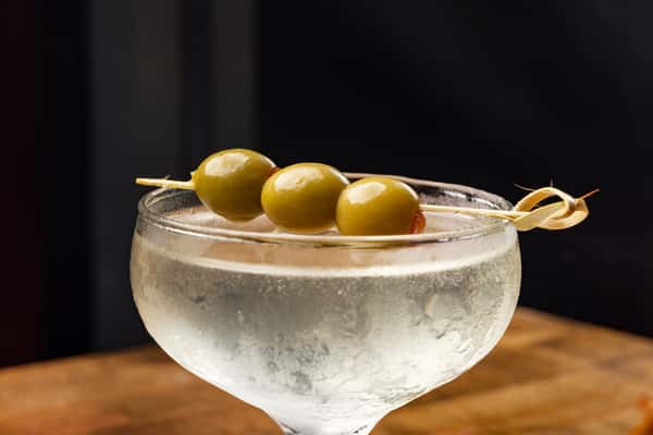 Classic dirty martini served in a chilled coupe glass, garnished with three green olives on a cocktail skewer.