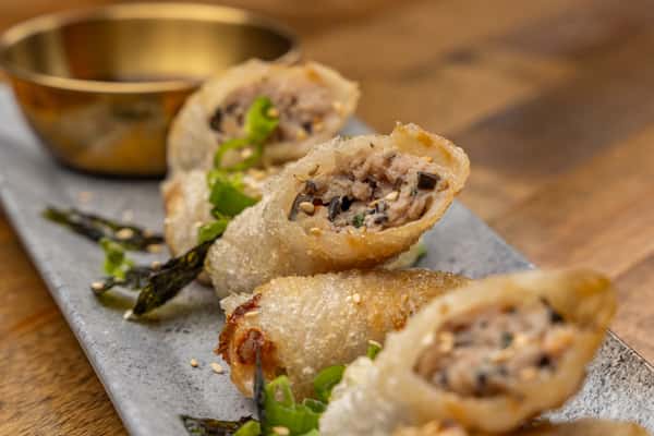 Crispy Vietnamese-style spring rolls filled with savory minced pork, herbs, and glass noodles, served with dipping sauce and garnished with scallions and sesame seeds.