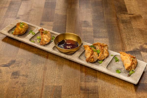 Crispy fried dumplings arranged on a long stone platter, garnished with scallions and paired with a savory soy-based dipping sauce.