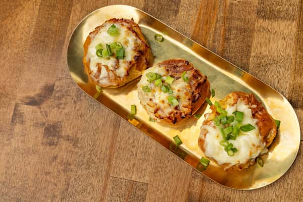 Baked cheesy rolls topped with melted mozzarella and sliced green onions, served on a golden tray for a savory appetizer option.