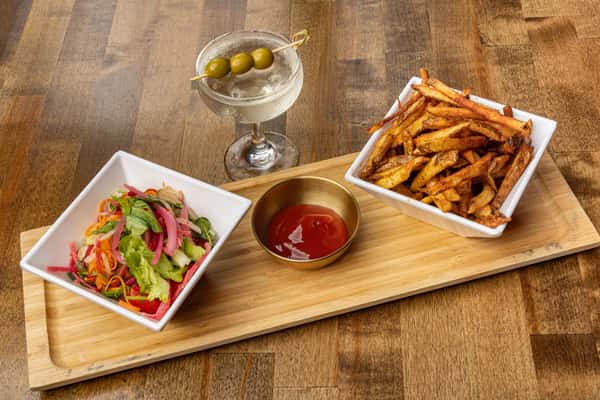 Trio of appetizers including a fresh garden salad with pickled onions, crispy hand-cut fries, and a chilled martini with olives, served on a wooden platter with ketchup.