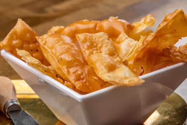 Crisp and golden fried wonton chips served in a square white bowl, ideal for dipping or snacking in an upscale Asian fusion setting.