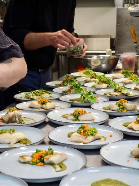 A cook prepares white fish dishes in a restaurant kitchen. The plates are lined up and garnished with vegetables.