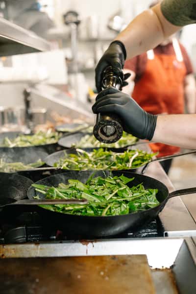 A person with black gloves adding pepper to a dish