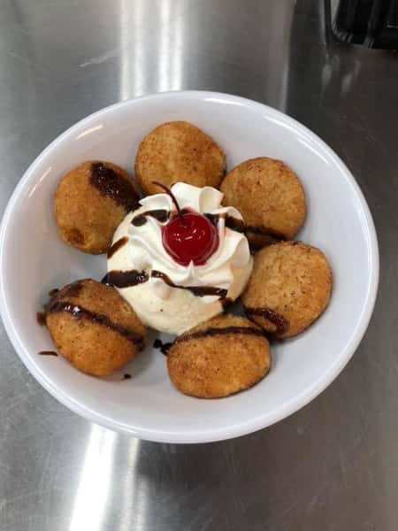 Fried dessert with scoop of ice cream topped with whipped cream and cherry in center
