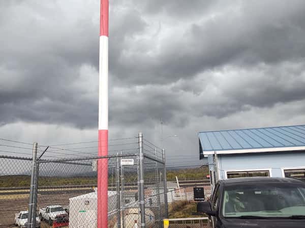 Exterior view of Crosswinds Restaurant in Payson, Arizona, beside an airport runway with stormy skies, barbed wire fencing, and parked vehicles.