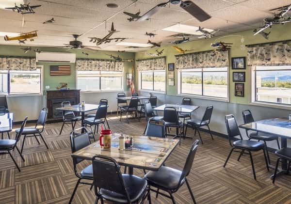 Interior of Crosswinds Restaurant with aviation-themed decor, featuring hanging model airplanes and large windows offering scenic runway views at Sedona Airport.
