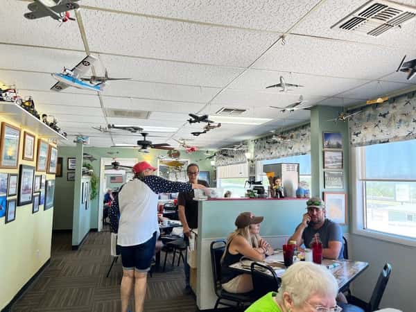Interior of Crosswinds Restaurant in Payson, AZ, decorated with hanging model airplanes and aviation-themed artwork, as guests enjoy casual dining.
