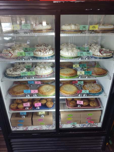 Refrigerated display case filled with assorted homemade pies, cream-topped desserts, and muffins at Crosswinds Restaurant, each labeled with colorful tags.