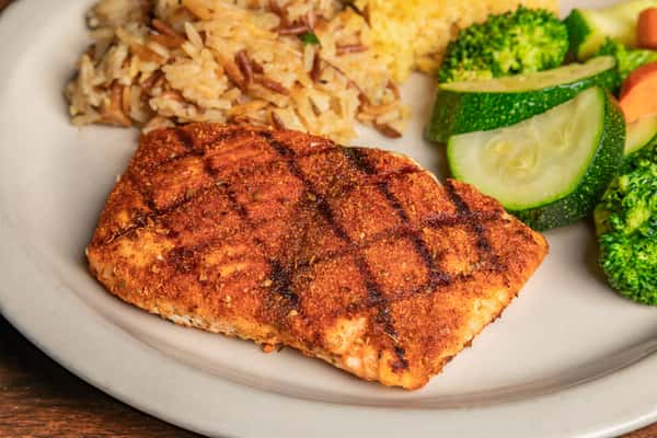 Grilled salmon filet served with seasoned rice pilaf and steamed broccoli, zucchini, and carrots.