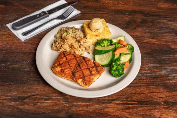 Grilled salmon served with seasoned rice, steamed vegetables, and cornbread topped with a scoop of butter.