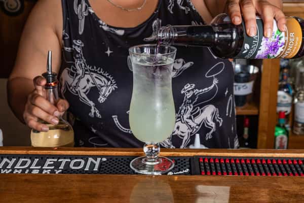 Lavender syrup being poured into a tall iced lemonade by a bartender wearing a cowboy print shirt at a Pendleton Whisky bar.