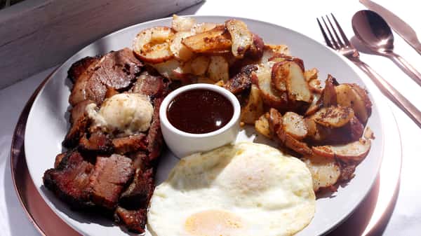 Steak and eggs plate with breakfast potatoes and a small cup of sauce.