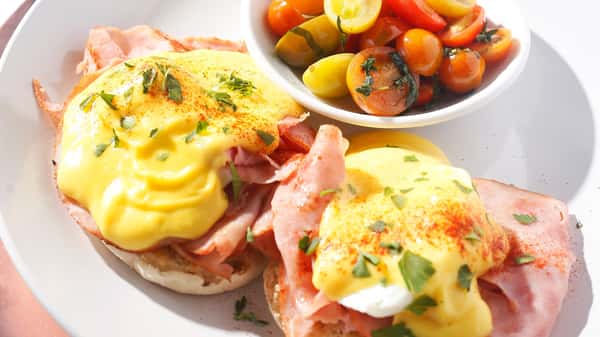 Eggs Benedict with ham, hollandaise sauce, and cherry tomatoes.