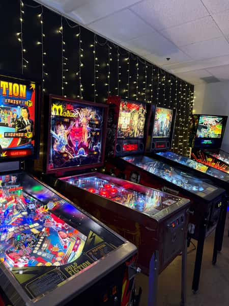 A row of lit-up pinball machines in the Teachers Lounge Arcade at Schoolhouse Brewing, including Pulp Fiction, Medusa, The Walking Dead, and Game of Thrones