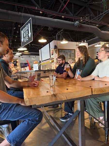Friends sharing beers and talking around a long wooden table in the Schoolhouse Brewing taproom