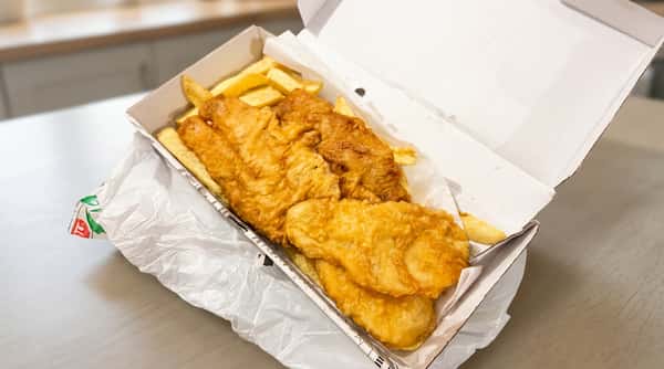 Golden battered fish and chips served in a takeaway box at Blue Bay in Glasgow.