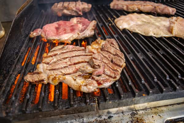Assorted steaks and chicken grilling over open flames—authentic Latin American barbecue preparation for bold, smoky flavor.