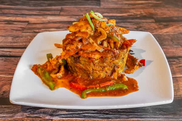 Traditional mofongo served on a white plate, topped with a rich, savory seafood and onion creole sauce, garnished with bell peppers and scallions—an iconic Puerto Rican and Dominican dish full of bold Caribbean flavors.