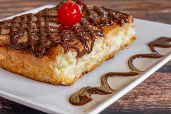 Creamy tres leches cake slice topped with chocolate drizzle and a maraschino cherry—decadent Caribbean dessert with a sweet finish.