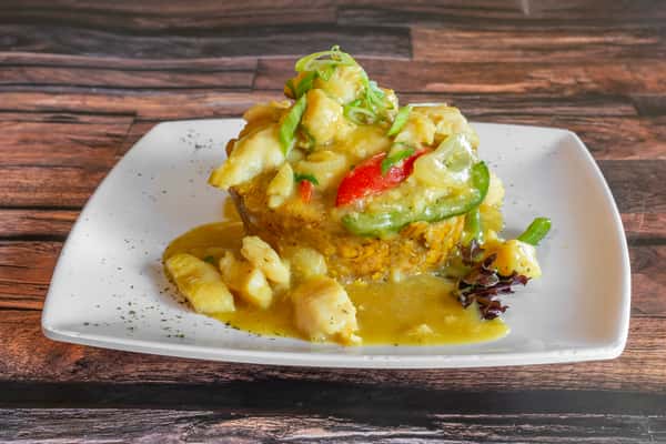 Traditional mofongo drenched in a garlicky seafood broth with peppers and onions, featuring chunks of white fish—comforting Puerto Rican–Dominican fusion dish.