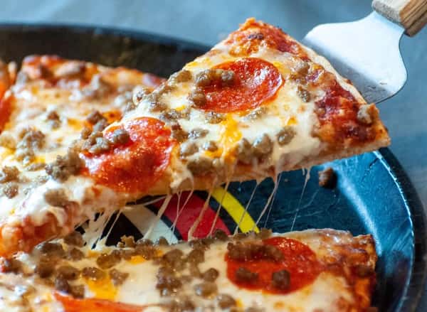A slice of pepperoni and sausage pizza being lifted from a tray, with melted cheese stretching from the rest of the pie.