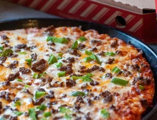 Philly cheesesteak pizza with chopped steak, green bell peppers, and melted mozzarella on a pan.