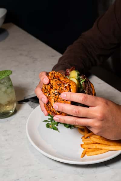 person holding a burger over plate at table