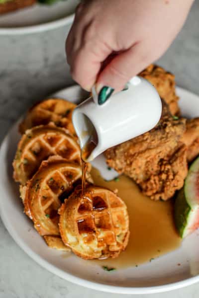 person pouring maple syrup over chicken and waffles